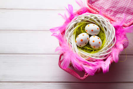 Easter eggs in the nest and pink basket on white wooden tableの写真素材