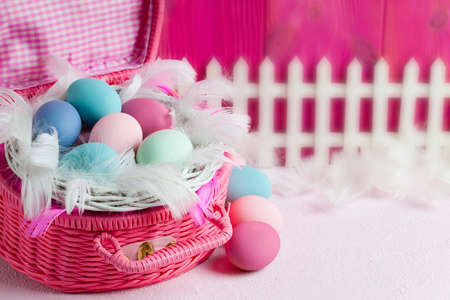 Colored Easter eggs in the nest, feathers and white fence on pink wooden backgroundの写真素材