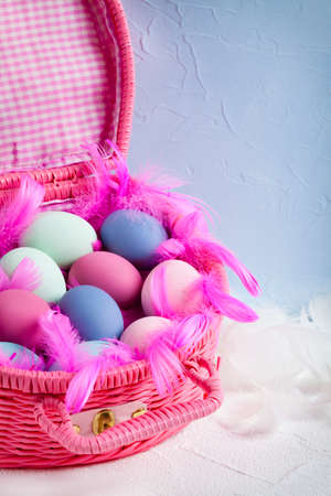 Happy Easter - pink basket full of colored eggs and feathers on blue and white backgroundの写真素材