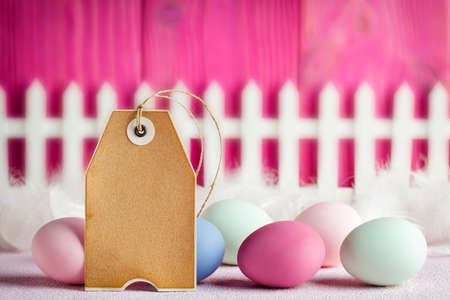 Paper label and colored Easter eggs and white fence on pink wooden planksの写真素材