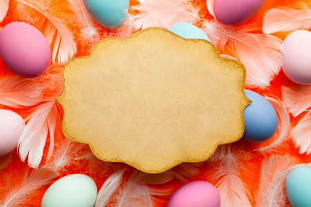 Blank paper label, colored Easter eggs and white feathers on orange backgroundの写真素材
