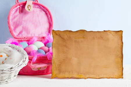 Blank paper sheet and pink basket full of colored eggs