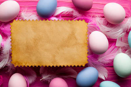 Blank paper sheet, colored Easter eggs and feathers on pink wooden backgroundの写真素材