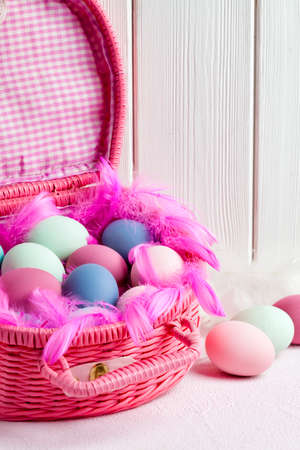 Happy Easter - pink basket full of colored eggs and feathers on white wooden backgroundの写真素材
