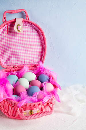 Happy Easter - pink basket full of colored eggs and feathers on blue and white backgroundの写真素材