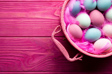 Colored Easter eggs and feathers in basket on pink wooden backgroundの写真素材
