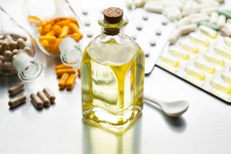 Medicine as a syrup in a glass bottle and various capsules on a metal tableの写真素材