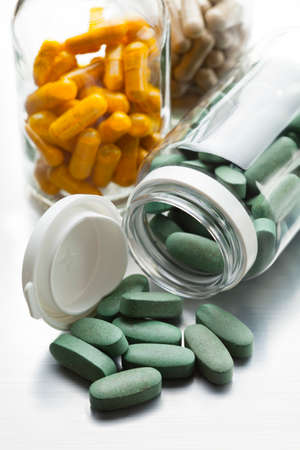 Green, yellow and brown tablets in glass bottles on gray tableの写真素材