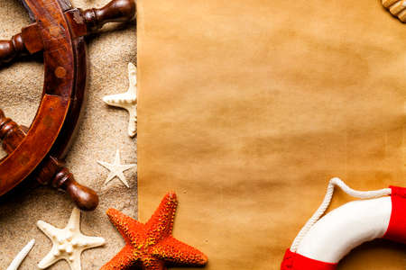 Blank handmade paper sheet, starfish, lifebuoy and ship's steering wheel on the beachの写真素材