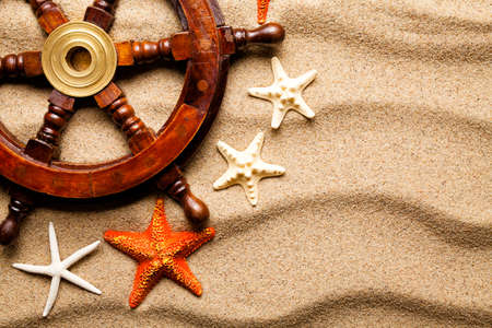 Ship's Steering Wheel and various starfish on beach sandの写真素材