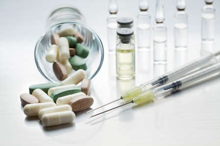 Two syringes and medicines in tablets and capsules on a metal tableの写真素材