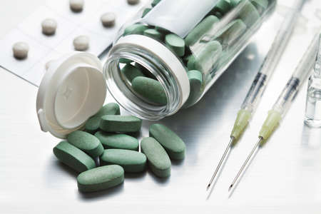 Green pills and two syringes with needles on a gray tableの写真素材