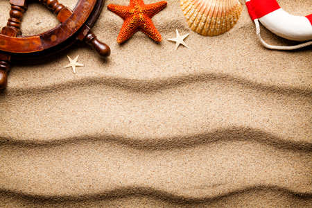 Summer beach background - ship's steering wheel, lifebuoy and shells on sand 