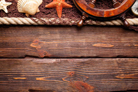 Marine background - fishing net, ship's steering wheel, hawser ans seashells on wooden boardの写真素材