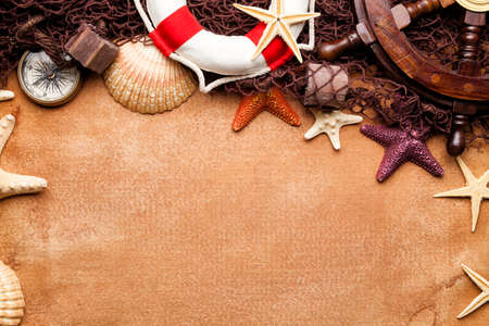 Ship's steering wheel, lifebuoy, compass, fishing net and seashells on paper backgroundの写真素材