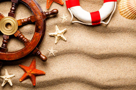 Lifebuoy, ship's steering wheel, various shell and starfish on beach sand backgroundの写真素材