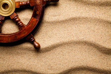 Wooden ship's steering wheel on beach sand backgroundの写真素材