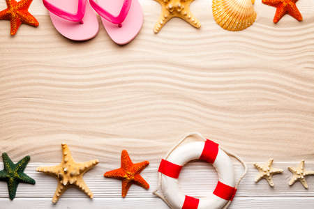 Summer background - shells, starfish, lifebuoy and flip flops on wooden plank and sand background