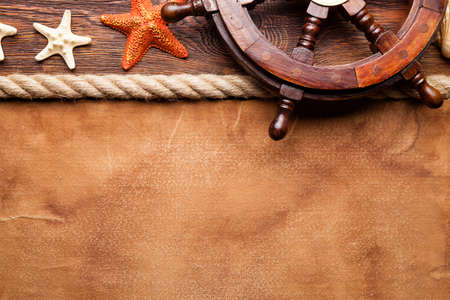 Ship's steering wheel, shell, starfish and hawser on paper and wooden backgroundの写真素材