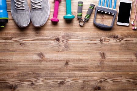 Fitness symbols and equipment - sneakers, water, dumbbell and smartphone with earphones on wooden backgroundの写真素材