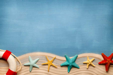 Summertime background - lifebuoy, beach sand and seashells on blue tableの写真素材