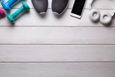 Fitness symbols - dumbbells, sports shoes and smartphone with headphones on a wooden backgroundの写真素材