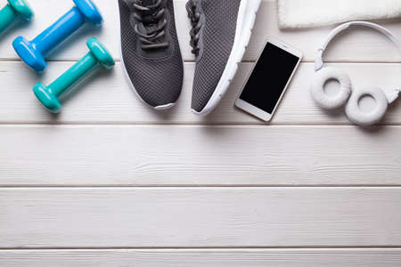 Fitness equipment - sports shoes, dumbbells, towel and smartphone with headphones on a wooden backgroundの写真素材