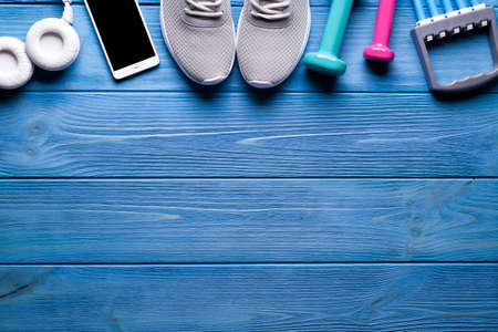 Fitness symbols - dumbbells, sports shoes and smartphone with headphones on blue wooden backgroundの写真素材