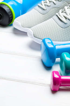 Sport and fitness symbols - sneakers, water and dumbbell on wooden wall background