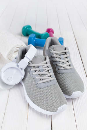 Sport symbols - gray sneakers, earphones, towel and dumbbells on white tableの写真素材