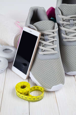 Smartphone, earphones, sport shoes, dumbbells and measuring tape on wooden boardの写真素材