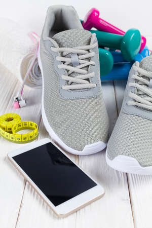Smartphone, earphones, sport shoes, dumbbells and measuring tape on wooden boardの写真素材