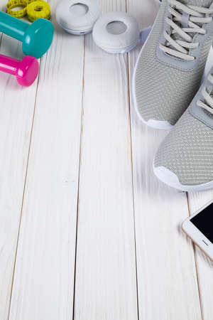 Gray sport shoes, dumbbells earphones and spartphone on wooden boardの写真素材