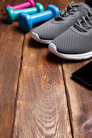 Smartphone, sport shoes and colored dumbbells on wooden tableの写真素材