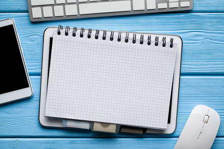 Notebook with copy space on digital tablet, smartphone, computer mouse and keyboard on blue wooden backgroundの写真素材