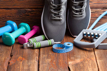 Various sports accessories - dumbbells, sport shoes and measuring tape on wooden backgroundの写真素材
