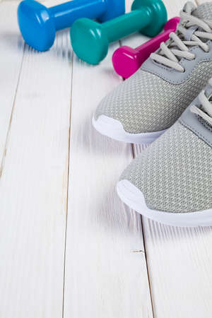 Colored dumbbells and gray sport shoes on white wooden tableの写真素材