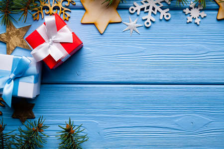 Two gift boxes, branch of spruce tree and wooden Christmas decorations, stars and snowflakes on blue wooden tableの写真素材
