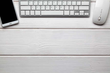 Smartphone, computer keyboard and mouse on white wooden tableの写真素材