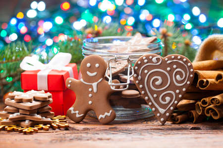 Red gift box and decorated gingerbread Christmas cookies on lighting colorful background and wooden tableの写真素材