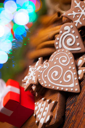 Red gift box and decorated gingerbread Christmas cookies on lighting colorful background and wooden tableの写真素材