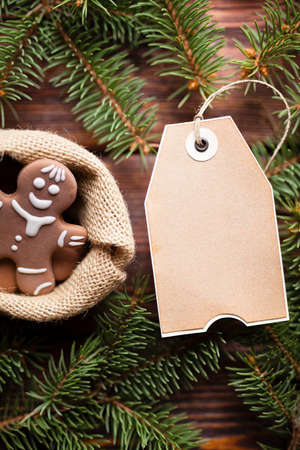 Christmas cookies in bag, blank paper label and spruce tree on wooden backgroundの写真素材