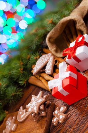 Red and white gift box and decorated gingerbread Christmas cookies on lighting colorful background and wooden tableの写真素材