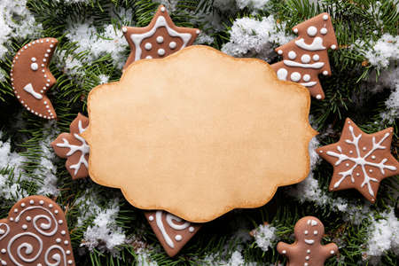 Blank paper card and gingerbread Christmas cookies on snow covered spruce branchの写真素材
