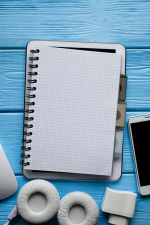 Notebook on tablet, smartphone and white earphones on blue wooden backgroundの写真素材