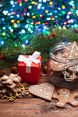 Decorated gingerbread Christmas cookies, gift box and branch of spruce tree with many colored lights on wooden tableの写真素材