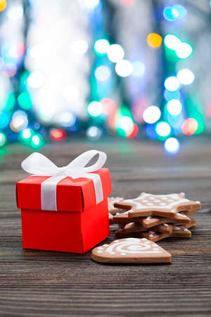 Red gift box with white ribbon and Christmas cookies on wooden table
