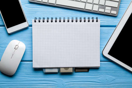 Notepad with copy space, smartphone, tablet and computer mouse and keyboard on blue tableの写真素材