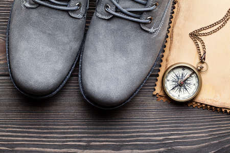 Pair of hiking boots, paper sheet and compass on wooden tableの写真素材