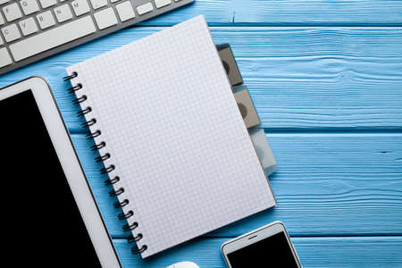 Notepad with blank paper sheet, digital tablet, smartphone and computer keyboard on blue wooden backgroundの写真素材